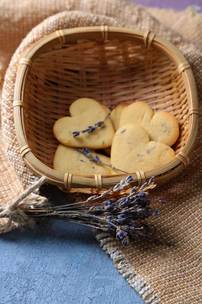 Лавандовое печенье в плетеной корзине, на мешковине, на цветном деревянном фоне — стоковое фото