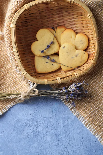 Biscotti di lavanda in cesto di vimini, su sacco, su sfondo di legno a colori — Foto Stock