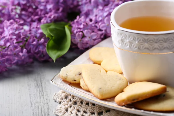 Лавандовое печенье и чашка вкусного чая на фоне цвета дерева — стоковое фото