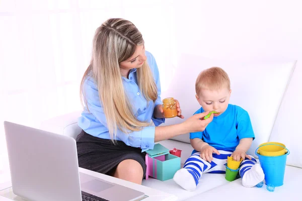 Jovem mãe bonita alimentando seu filho no sofá no quarto — Fotografia de Stock