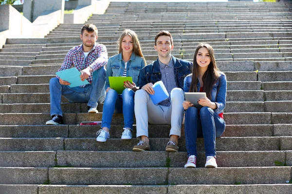 Zadowoleni uczniowie siedzący na schodach w parku — Zdjęcie stockowe