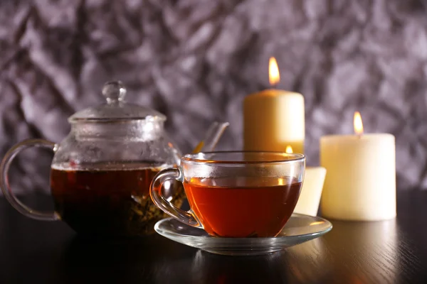 Složení s čajem ve skleněné konvici a svíčky na stole, na tmavém pozadí — Stock fotografie