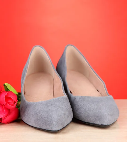 Mooie grijze vrouwelijke schoenen en bloemen op rode achtergrond — Stockfoto