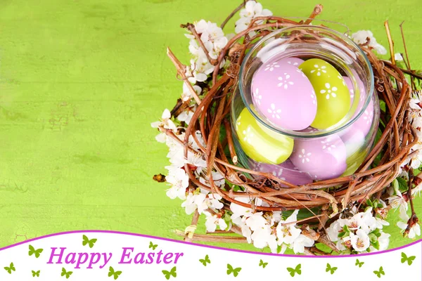 Composition with Easter eggs and blooming branches in glass jar and decorative nest, on  color wooden background — Stock Photo, Image