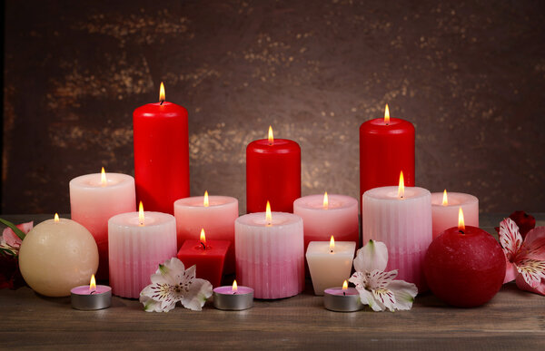 Beautiful candles with flowers on table on brown background