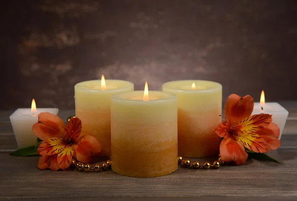 Mooie kaarsen met bloemen op tafel op bruine achtergrond — Stockfoto