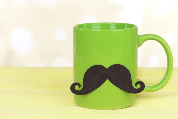 Cup with mustache on table on light background — Stock Photo, Image