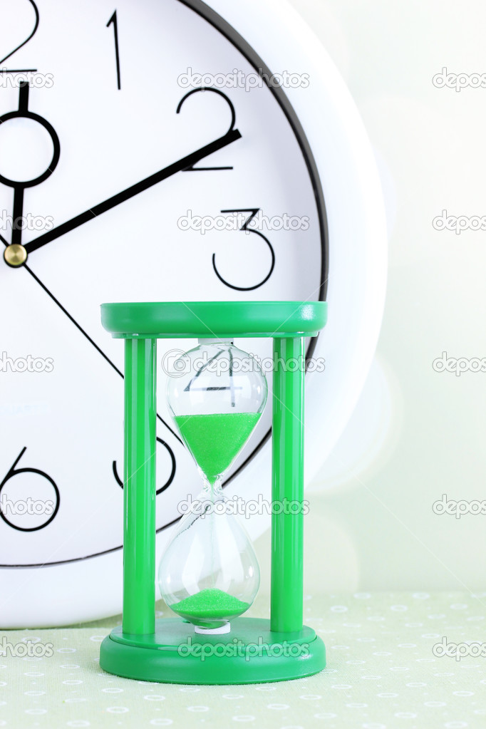 Hourglass and big clock on light background