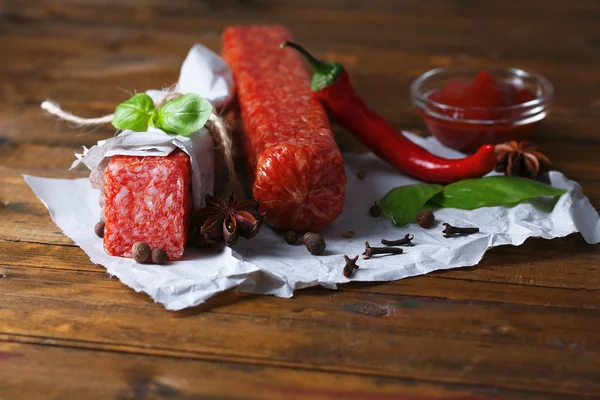 Tasty salami sausage and spices on wooden background — Stock Photo, Image