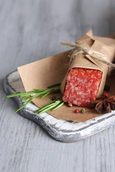 Tasty salami sausage, on paper on wooden background — Stock Photo, Image