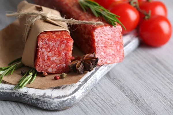 Leckere Salami-Wurst, Gemüse und Gewürze auf Papier Holzgrund — Stockfoto