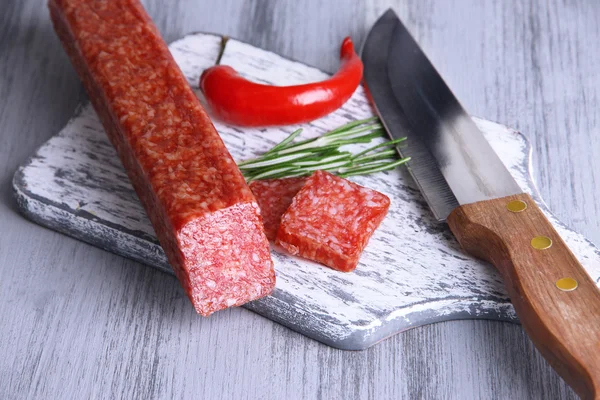 Tasty salami sausage, knife and spices on wooden background — Stock Photo, Image