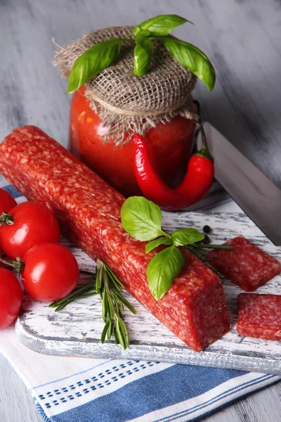 Tasty salami sausage, vegetables, knife and spices on wooden background — Stock Photo, Image