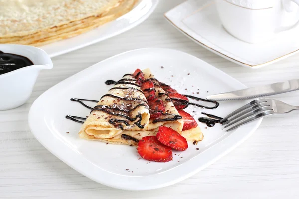 Deliciosas panquecas com morangos e chocolate no prato na mesa — Fotografia de Stock