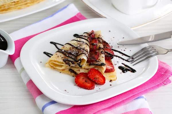Heerlijke pannenkoeken met aardbeien en chocolade op plaat op tafel — Stockfoto