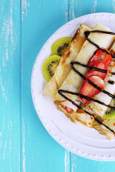 Leckere Pfannkuchen mit Erdbeeren und Schokolade auf dem Teller auf dem Tisch — Stockfoto