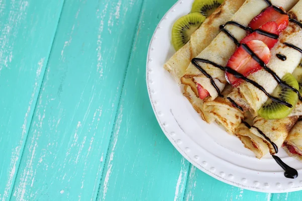 Leckere Pfannkuchen mit Erdbeeren und Schokolade auf dem Teller auf dem Tisch — Stockfoto