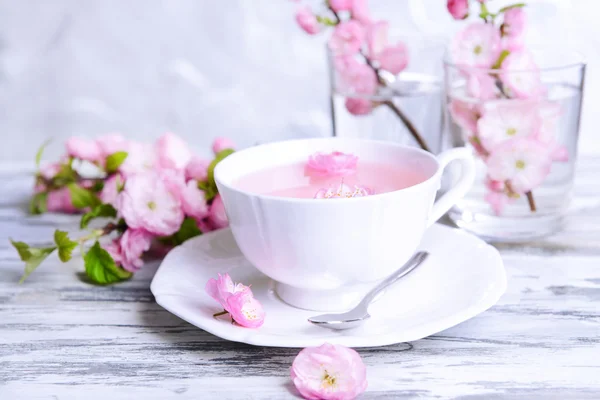 Beautiful fruit blossom with cup of tea on table on grey background