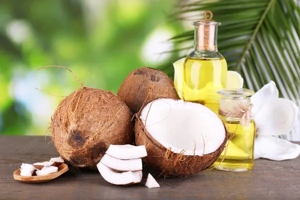 Orzechy kokosowe i olej kokosowy na drewnianym stole, na tle przyrody — Zdjęcie stockowe