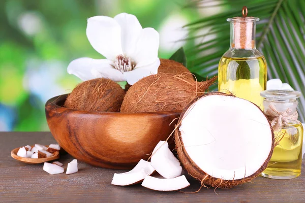 Noci di cocco e olio di cocco sul tavolo di legno, sullo sfondo della natura — Foto Stock