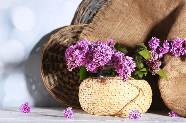 Lindas flores lilás em vaso de vime, na mesa de madeira cor, no fundo claro — Fotografia de Stock