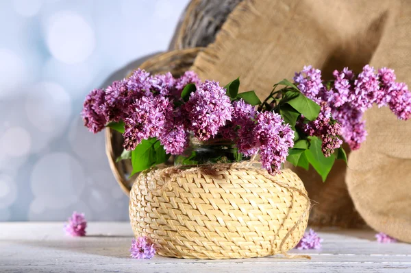 Bellissimi fiori lilla in vaso di vimini, su tavolo di legno a colori, su sfondo chiaro — Foto Stock