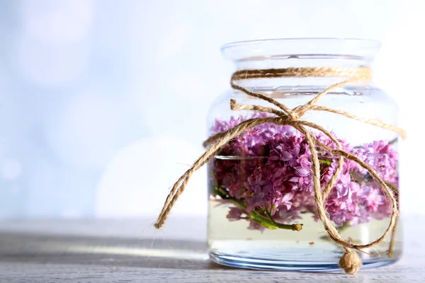 美丽的淡紫色花，在玻璃罐子里，颜色木制的桌子，在明亮的背景上 — 图库照片