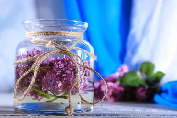 Lindas flores lilás em frasco de vidro, na mesa de madeira cor, no fundo brilhante — Fotografia de Stock