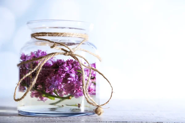 Bellissimi fiori lilla in vaso di vetro, su tavolo di legno a colori, su sfondo chiaro — Foto Stock