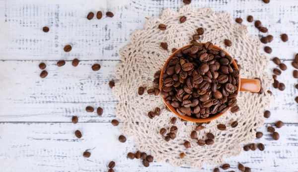 Copo cheio de grãos de café no fundo de madeira leve — Fotografia de Stock