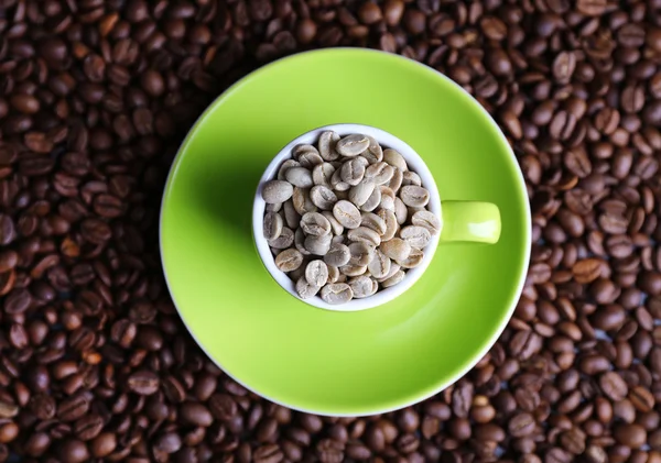Cup full of green coffee beans on brown coffee beans background