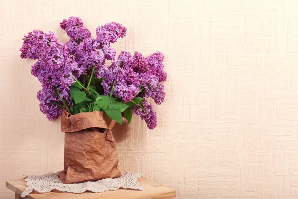 Красивые сиреневые цветы в бумажном пакете на деревянном столе у стены — стоковое фото