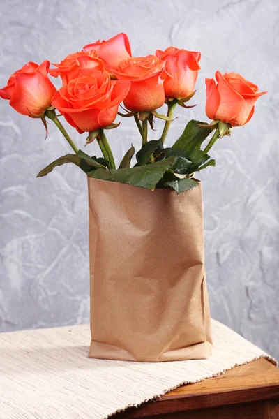 Beautiful roses in paper bag on wooden table near wall — Stock Photo, Image