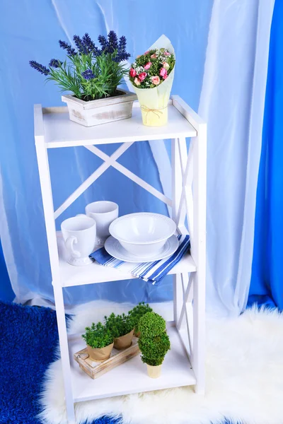 Красивые белые полки с посудой и декором на цветном фоне — стоковое фото