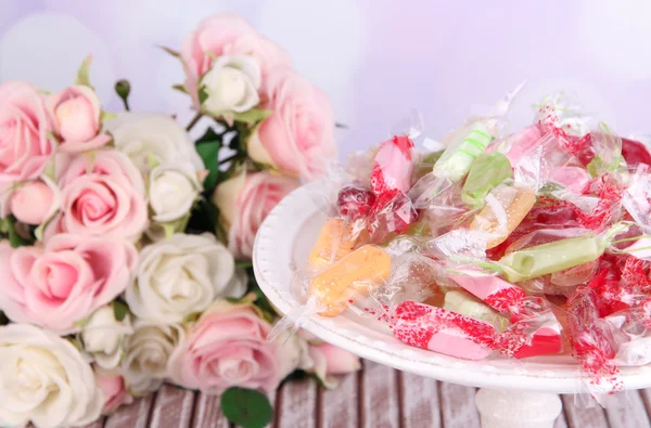 Sabrosos caramelos en plato con flores en la mesa sobre fondo brillante —  Fotos de Stock