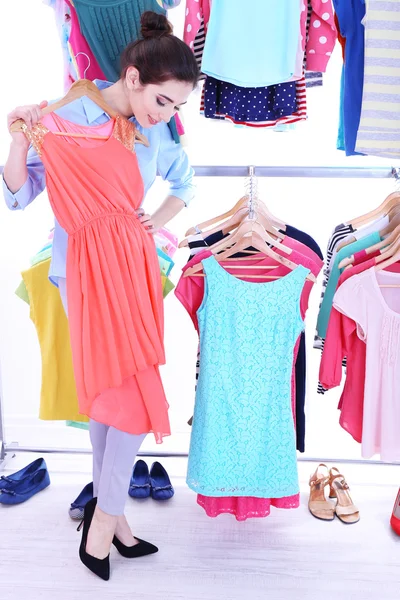 Junge Frau wählt Kleidung in der Nähe von Kleiderständern mit Kleiderbügeln — Stockfoto