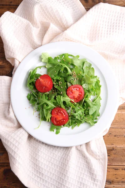 Salada verde feita com arugula, tomates e gergelim na placa, no fundo de madeira — Fotografia de Stock