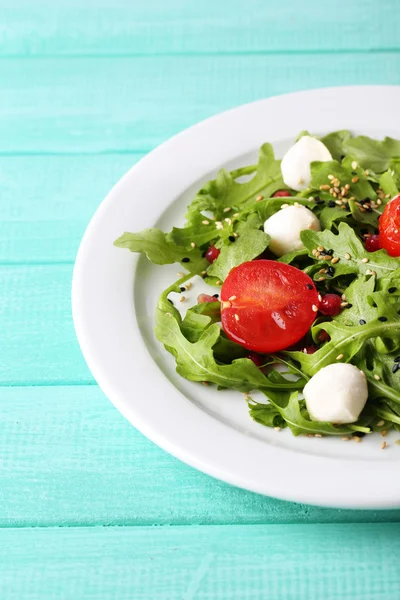 Grön sallad med rucola, tomater, ost mozzarella bollar och sesam på plattan, färg trä bakgrund — Stockfoto