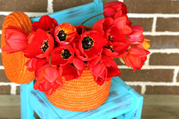 Букет разноцветных тюльпанов в плетеной корзине, на стуле, на домашнем фоне интерьера — стоковое фото