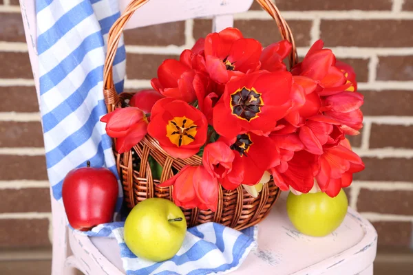 Bouquet of colorful tulips in wicker basket, on chair, on home interior background — Stock Photo, Image