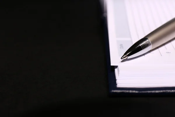 Pero na otevřenou knihu na černém stole, zblízka — Stock fotografie