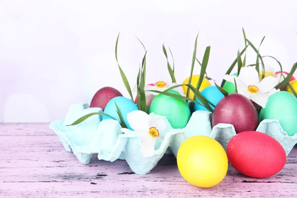 Huevos de Pascua coloridos con hierba y flores en bandeja sobre la mesa sobre fondo brillante — Foto de Stock