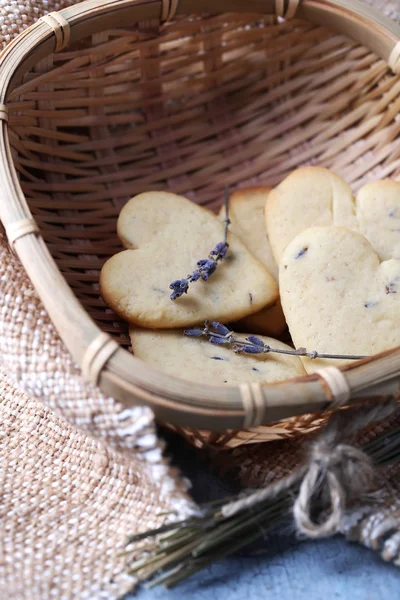 Galletas de lavanda en canasta de mimbre, sobre tela de saco, sobre fondo de madera de color — Foto de Stock