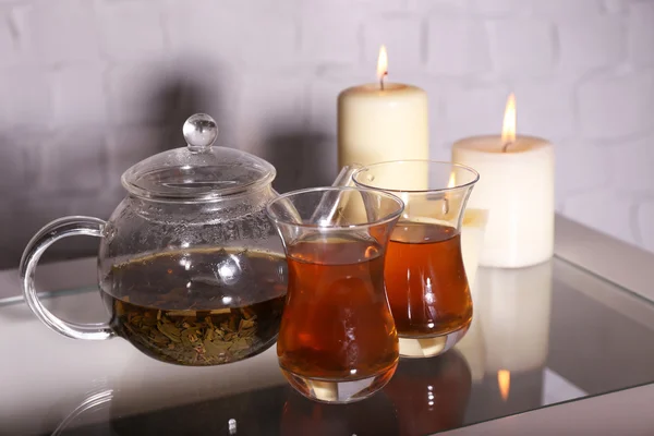 Kompozycja z herbaty szklany czajniczek i świece na stole, na jasnym tle — Zdjęcie stockowe