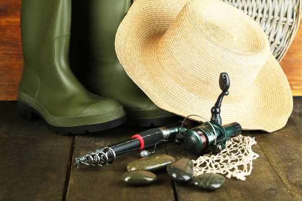 Рыболовный прут, резиновые сапоги и шляпа на деревянном столе крупным планом — стоковое фото
