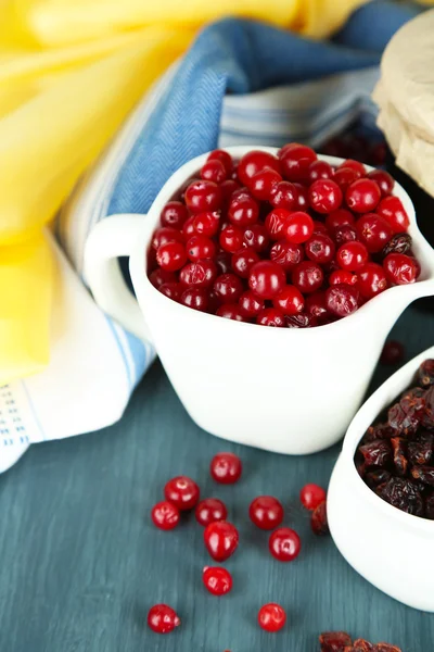 Fresh and dry cranberry in pitchers and bowl on wooden table close-up — Stock Photo, Image