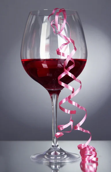 Copa de vino tinto y serpentina después de la fiesta sobre fondo gris —  Fotos de Stock
