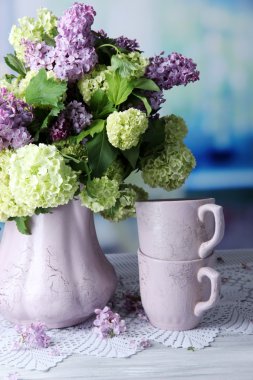 Çay bardağı ve güzel bahar çiçekleri parlak zemin üzerine ahşap masa üzerinde vazoda kompozisyonu