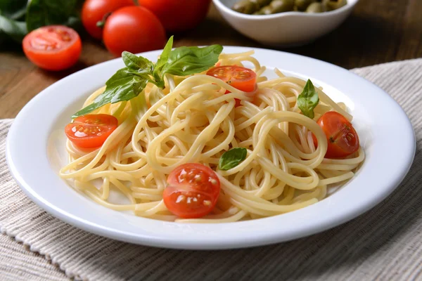 Deliciosos espaguetis con tomates en plato en la mesa de primer plano —  Fotos de Stock