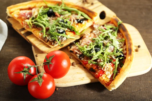 Stück Pizza mit Rucola auf Schneidebrett, auf farbigem Holzhintergrund — Stockfoto